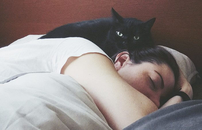 Un chat noir reposant sur le dos d'une personne endormie.
